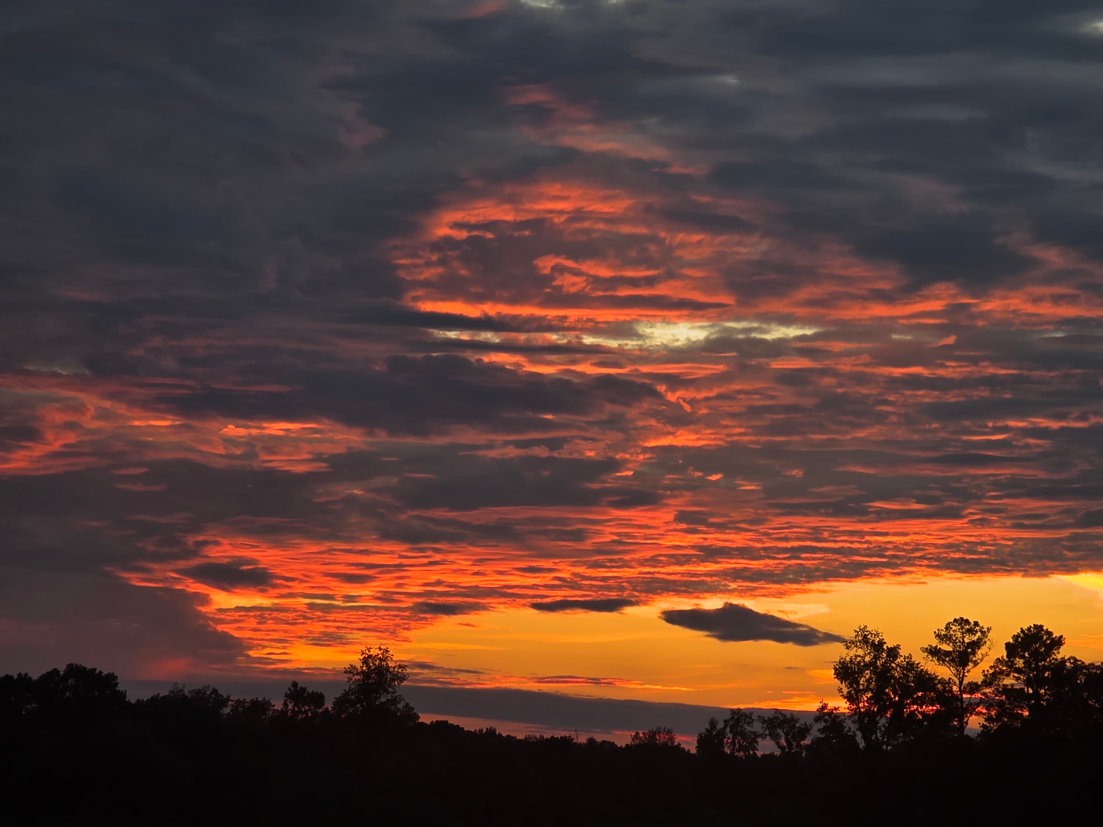 Amber Ridge — wide gradient sky of fire-orange clouds burning over a low silhouetted ridgeline at dusk.